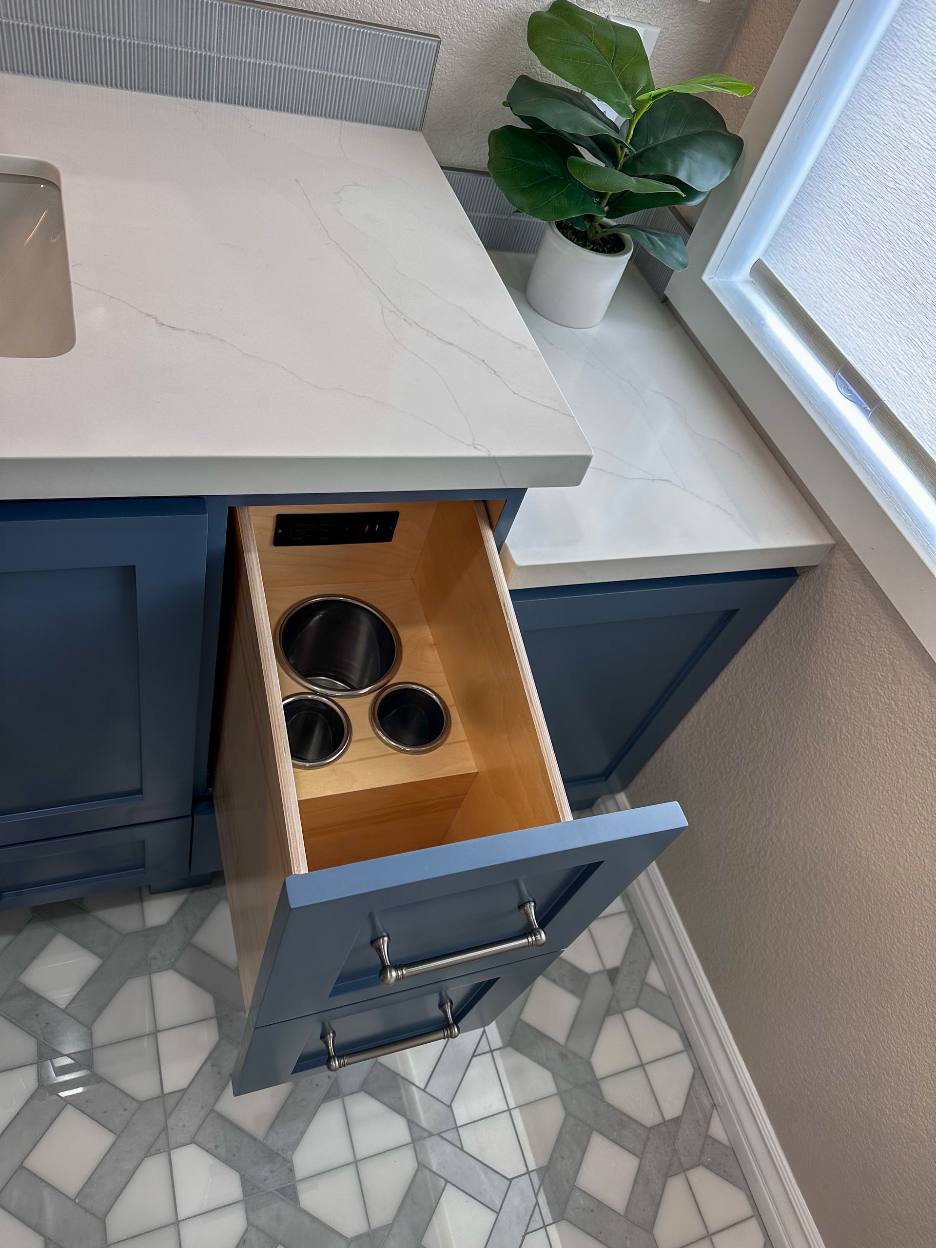 A pull-out vanity drawer with built-in metal canisters for storing hot styling tools, set in a blue cabinet.