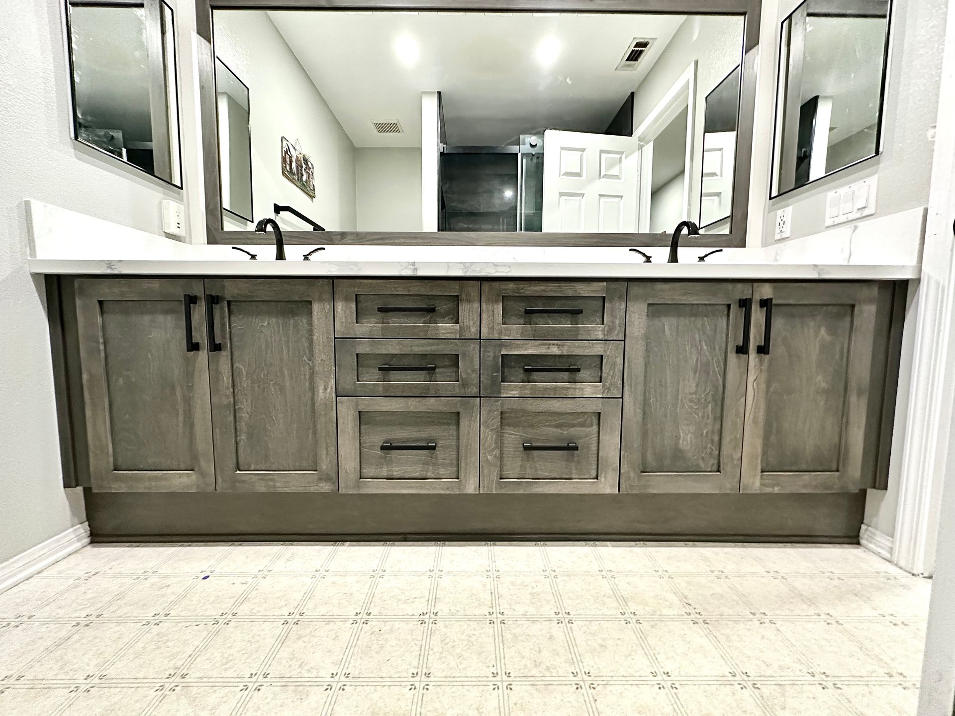 A double vanity with a wooden gray cabinet, white countertop, two black faucets, and large rectangular mirrors above.
