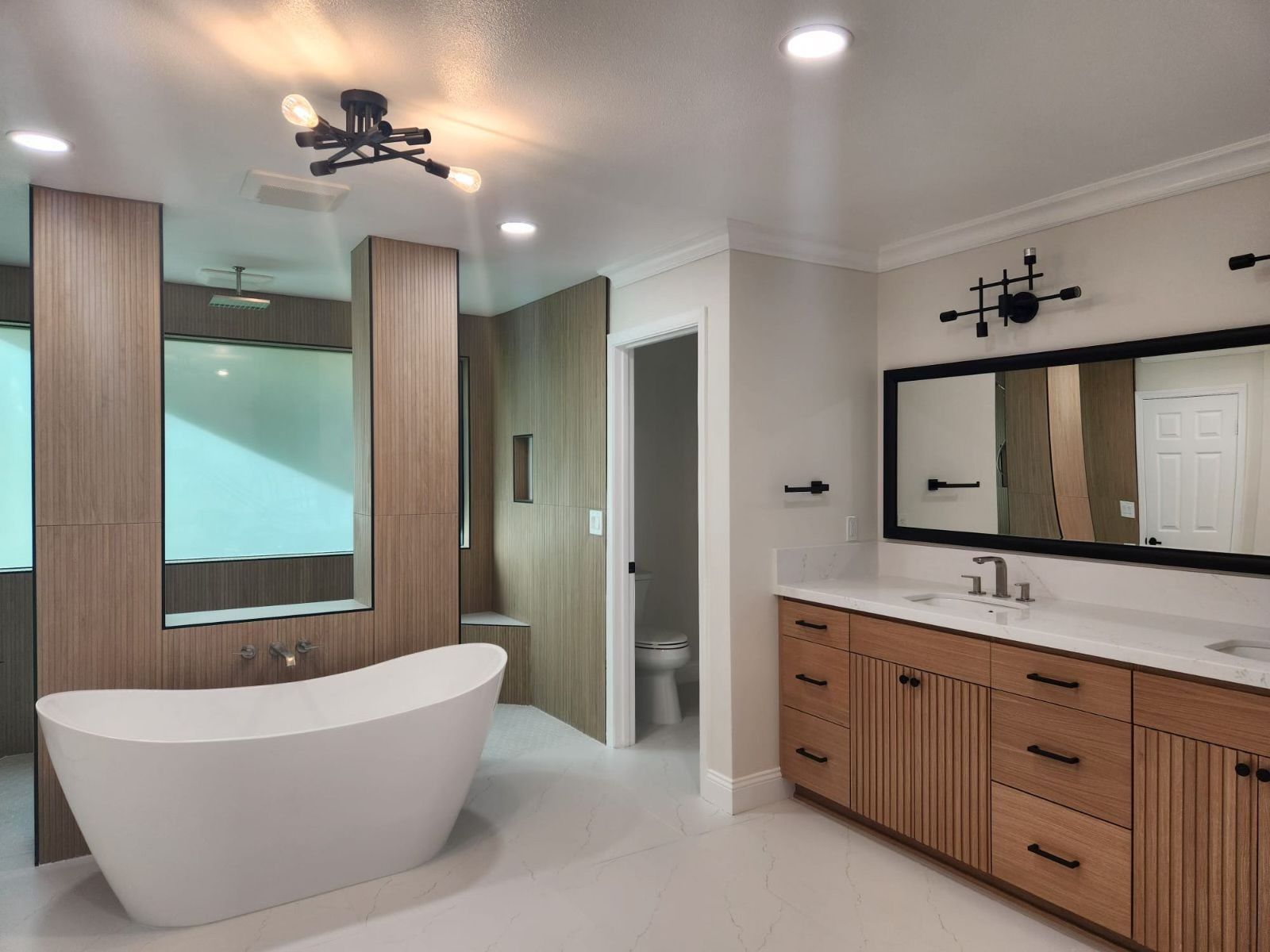 A modern bathroom featuring a white freestanding tub, wood-panel accent wall, and a wooden double vanity with black mirrors.