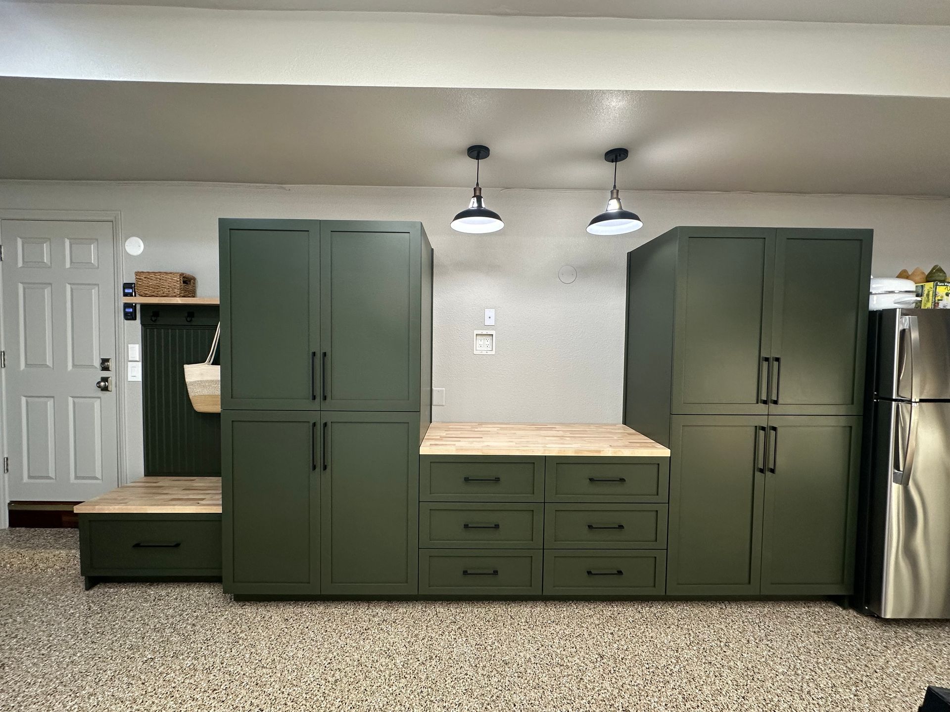 Custom olive green cabinetry with a wooden countertop and hanging lights installed along a wall in a garage.