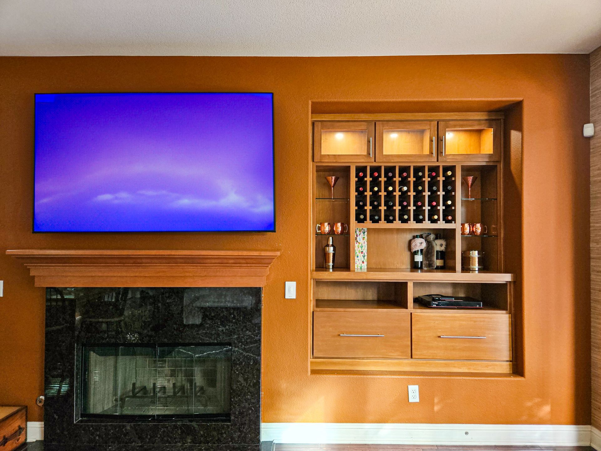 A fireplace with a large wall-mounted TV above it, next to a built-in wooden cabinet featuring wine storage and lighting.