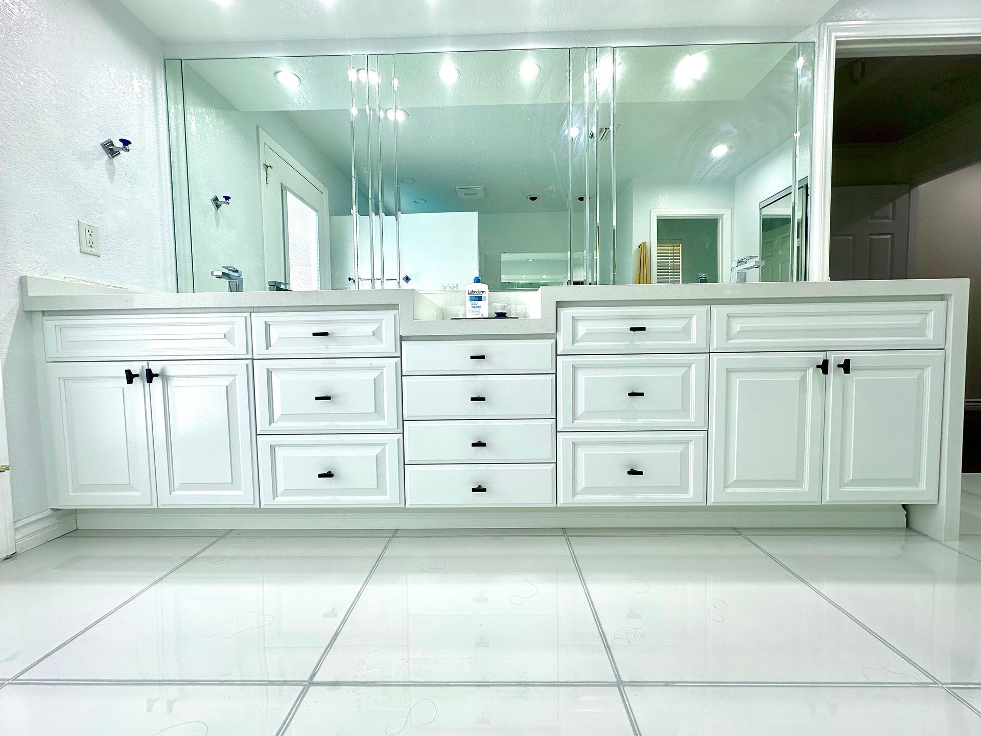 A white double bathroom vanity with cabinets and drawers, positioned beneath a large mirror on a tiled floor.