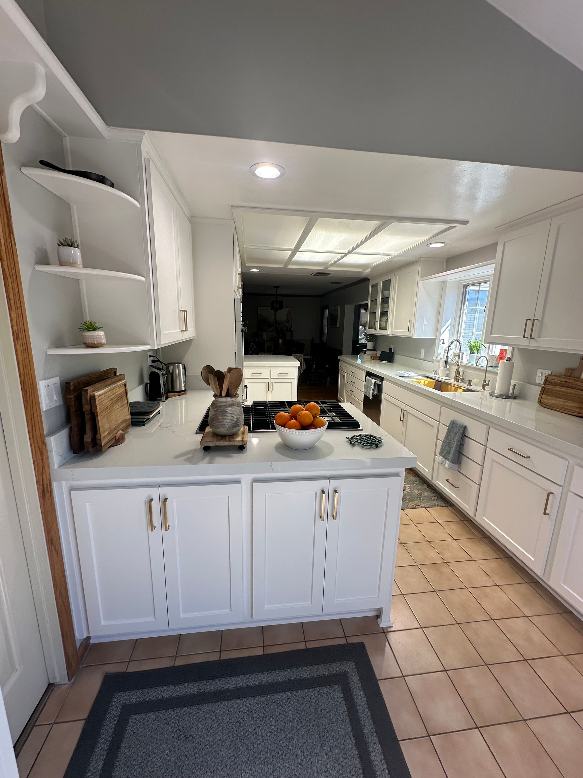 A bright kitchen with white cabinets, light countertops, open shelving, and a patterned tiled floor.