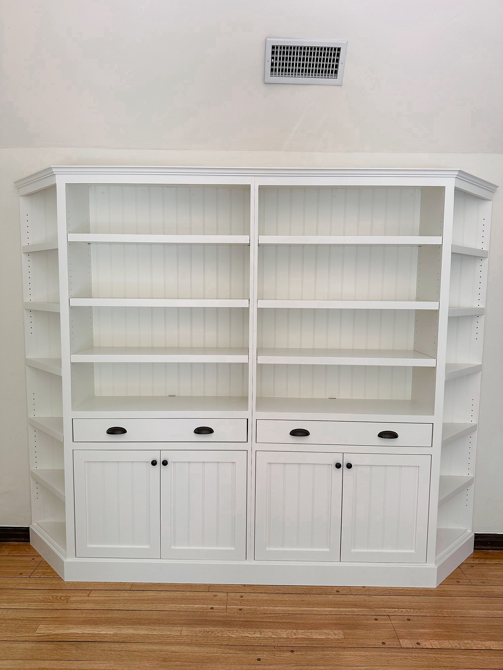 A white, farmhouse-style wooden bookshelf with two cabinets, four drawers, and open shelving, positioned against a wall.