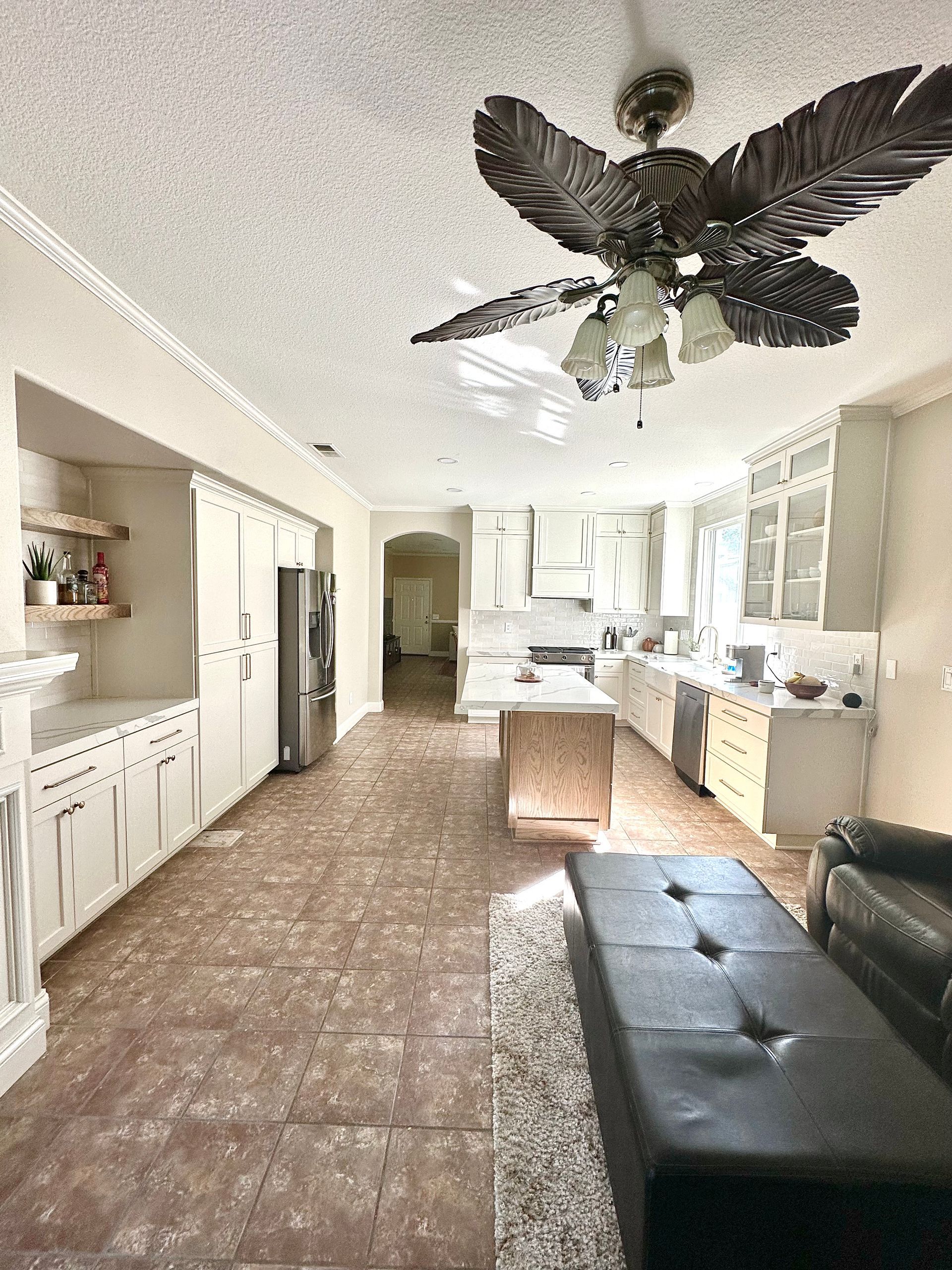 Spacious open-concept kitchen and living area with a decorative leaf-style ceiling fan and large tiled floors.