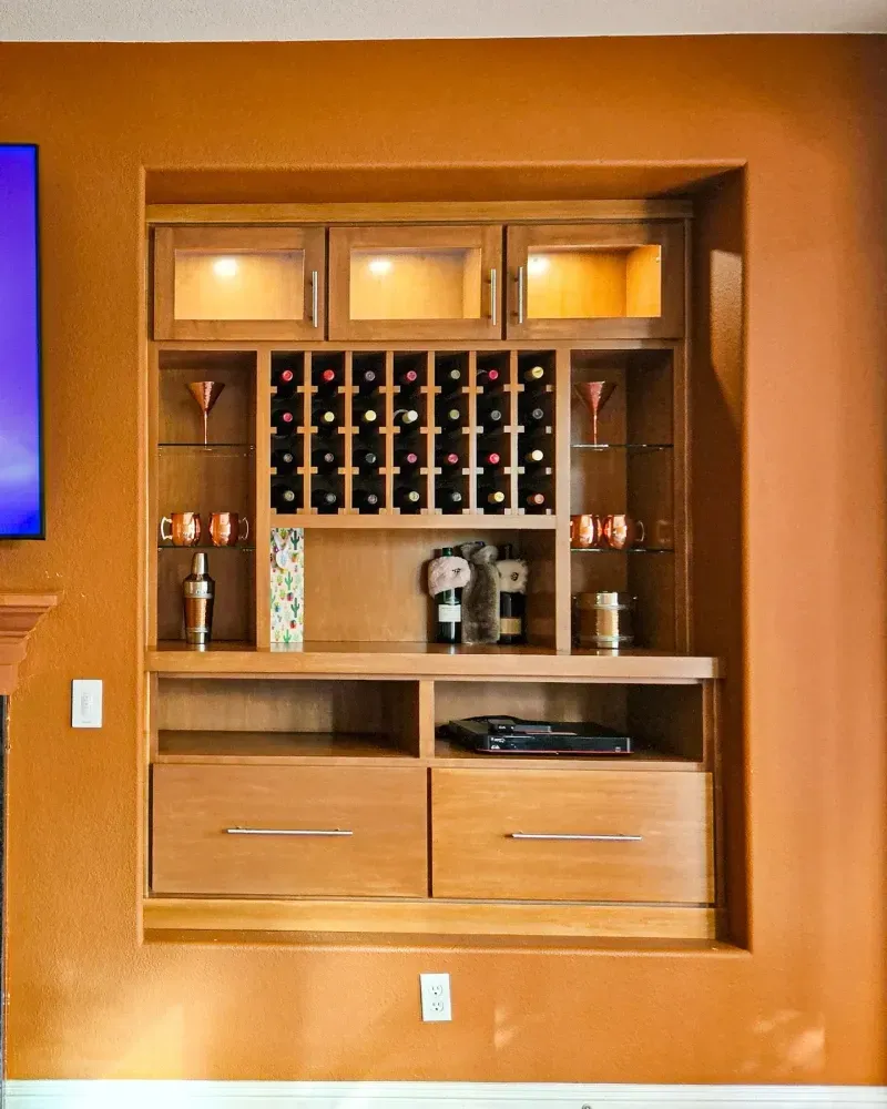 Built-in light wood cabinet with a wine rack, glass shelves, and two drawers, set into a wall painted orange.