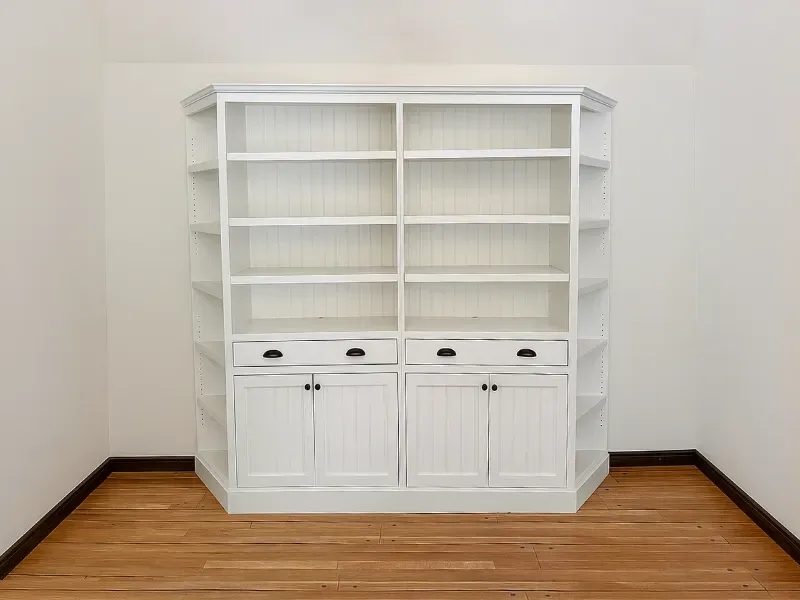 White wooden built-in bookshelf with central cabinet storage and drawers, positioned against a plain wall.