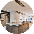 Modern kitchen with a wooden island, grey countertop, and a sleek rectangular pendant light, view into a living room.