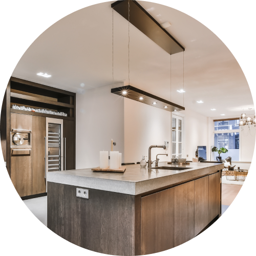Modern kitchen with a wooden island, grey countertop, and a sleek rectangular pendant light, view into a living room.