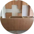 Unfinished kitchen featuring light wood cabinets and an island base in a room with white walls and a bare floor.
