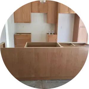 Unfinished kitchen featuring light wood cabinets and an island base in a room with white walls and a bare floor.
