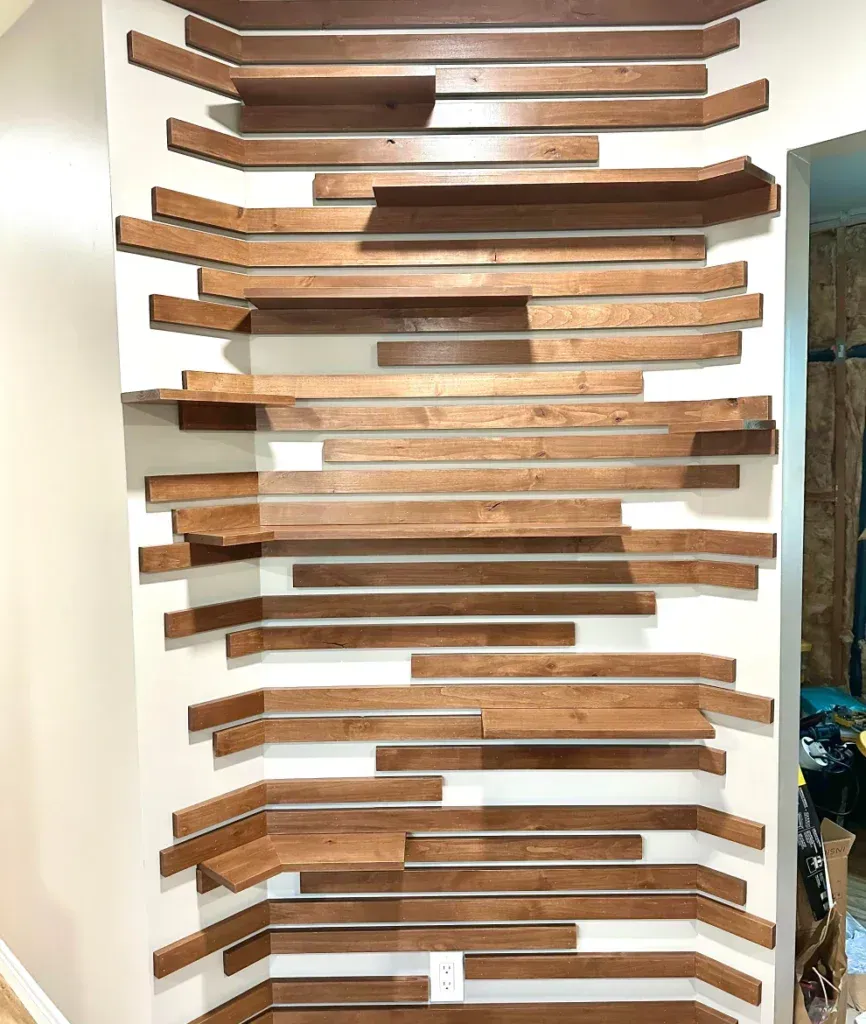 A wall installation featuring staggered, horizontal wooden planks in varying lengths, creating a layered, shelf-like effect.