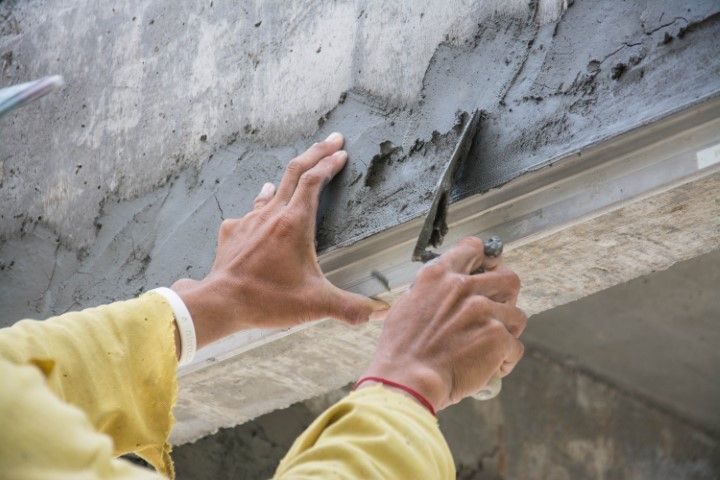 Hands using a trowel to smooth wet concrete on a wall edge