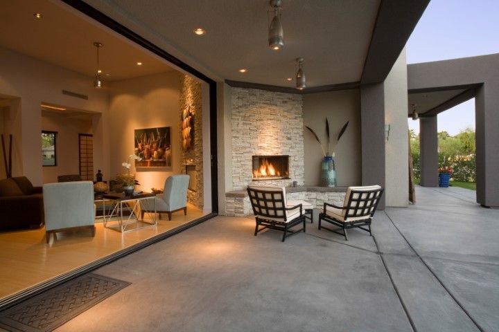 Modern patio with outdoor seating by a fireplace, opening to a warmly lit living room.