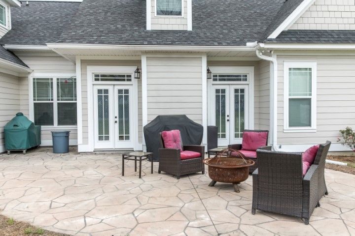 Back patio with wicker chairs, pink cushions, fire pit, and glass doors on a gray house.