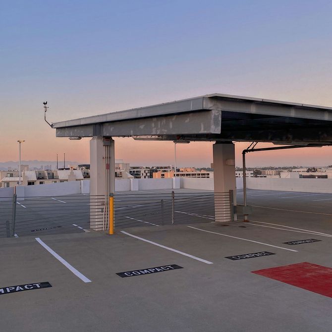 Empty rooftop parking area at sunset with concrete canopy, white parking lines, and red-marked space