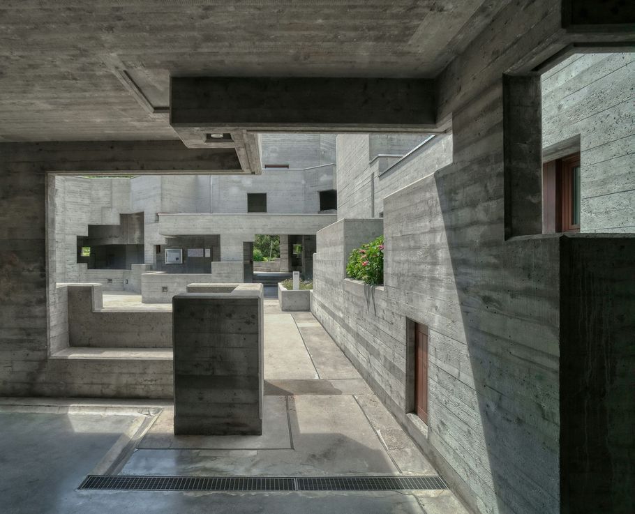 Modern concrete courtyard with geometric balconies and small green plants.