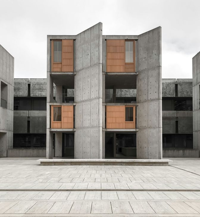 Modern concrete apartment facade with orange wooden shutters and a minimalist courtyard foreground