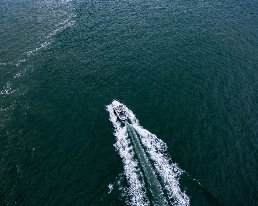 Boat traveling on dark blue water, leaving a white wake behind.