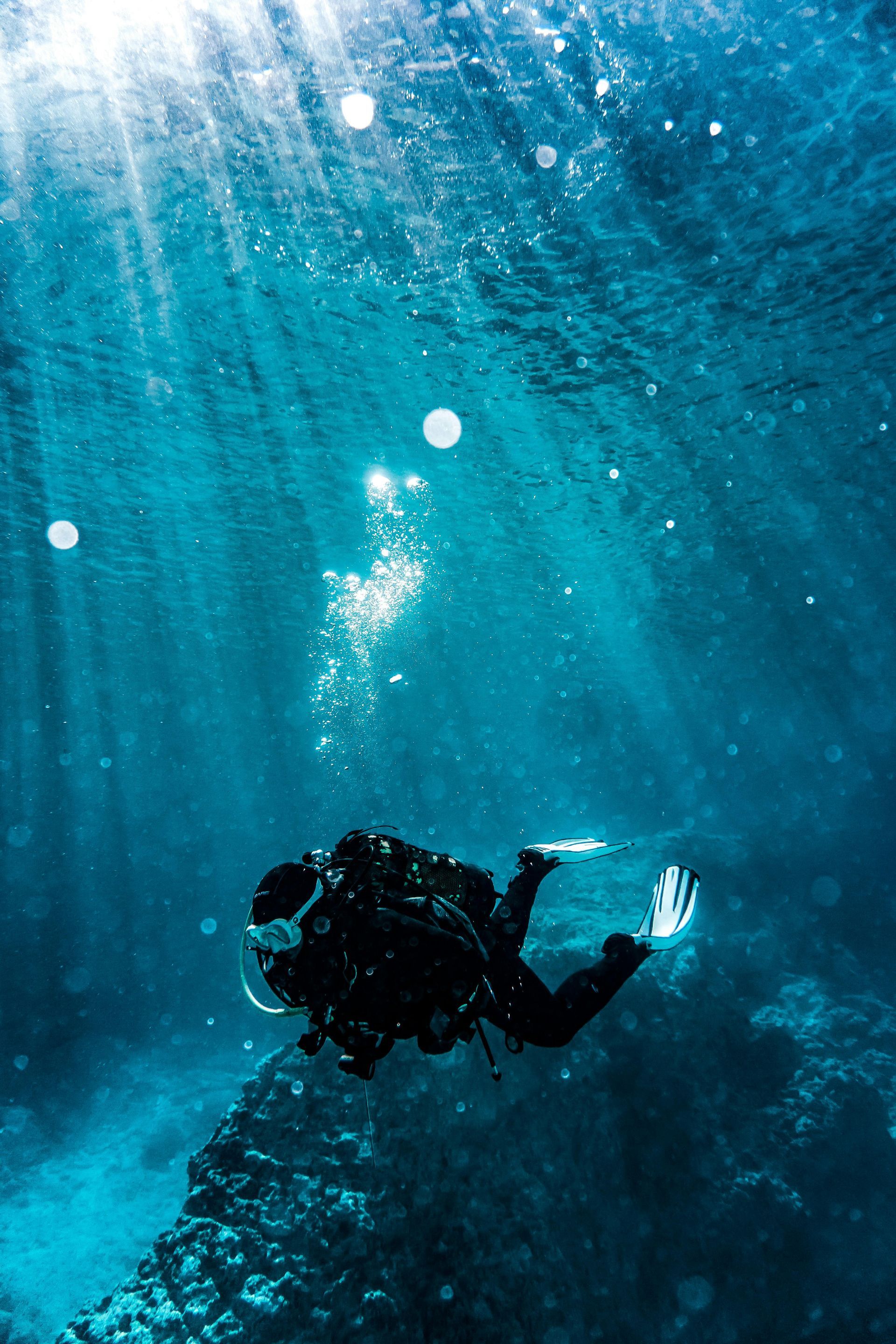 Scuba diver exploring underwater, illuminated by beams of sunlight filtering through the turquoise water.