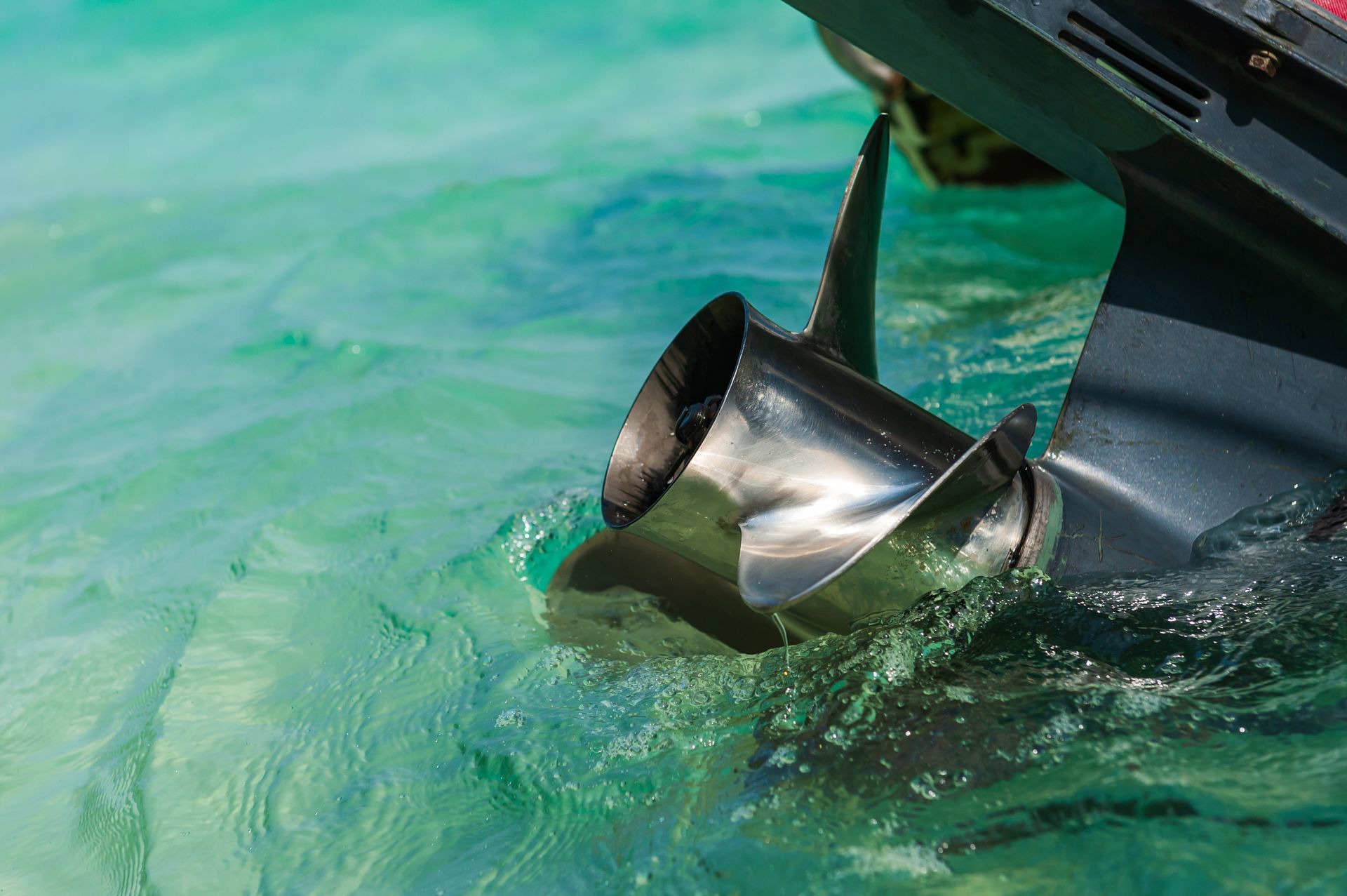Boat propeller churning water; stainless steel blades; turquoise water.