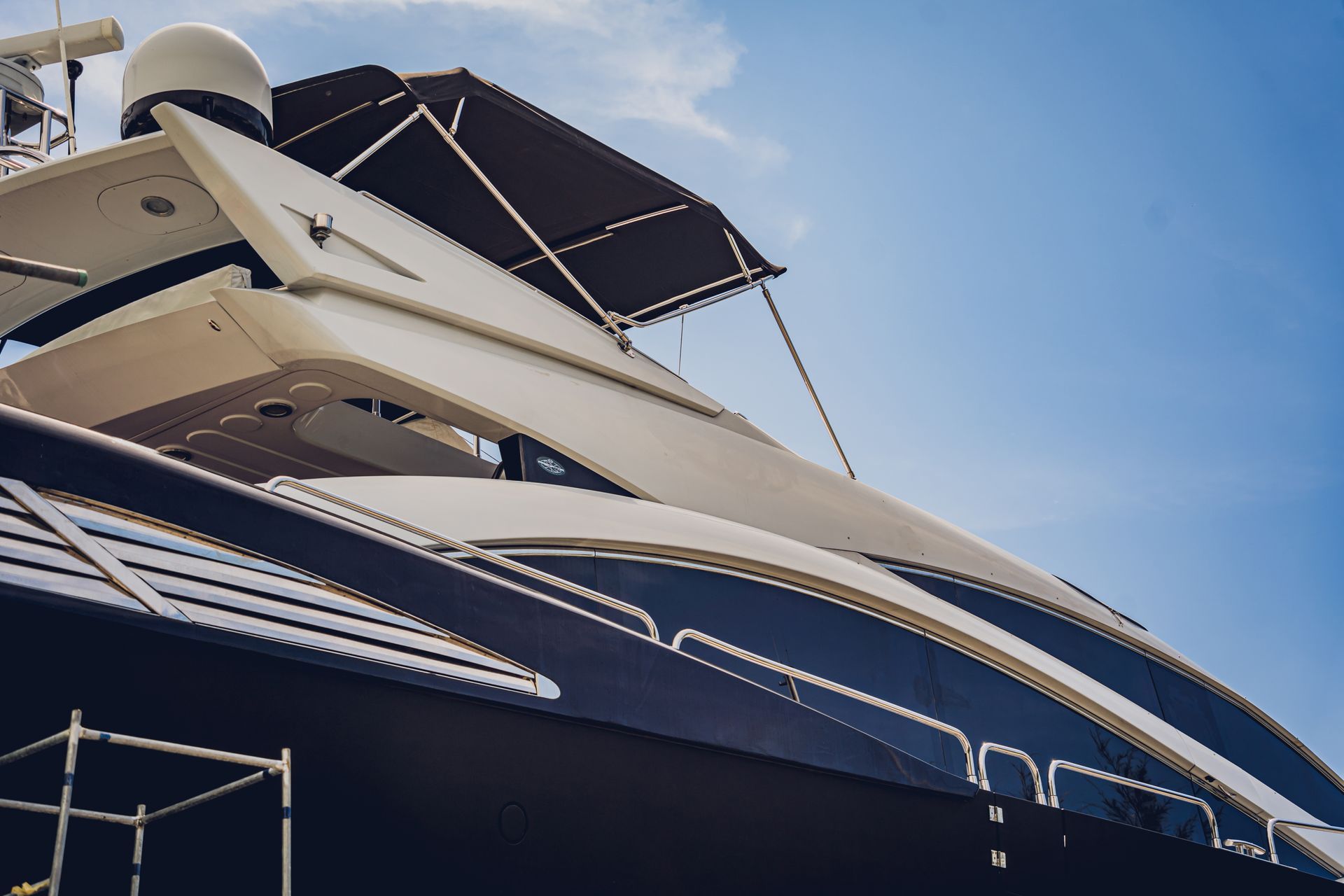 A large, dark blue yacht with a white top deck and radar, against a bright blue sky.