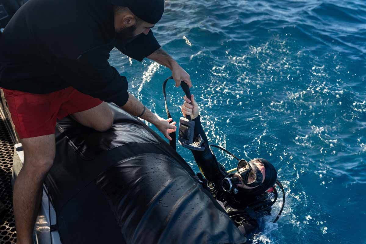 A rigid inflatable boat with multiple people in it on blue water under a clear sky.