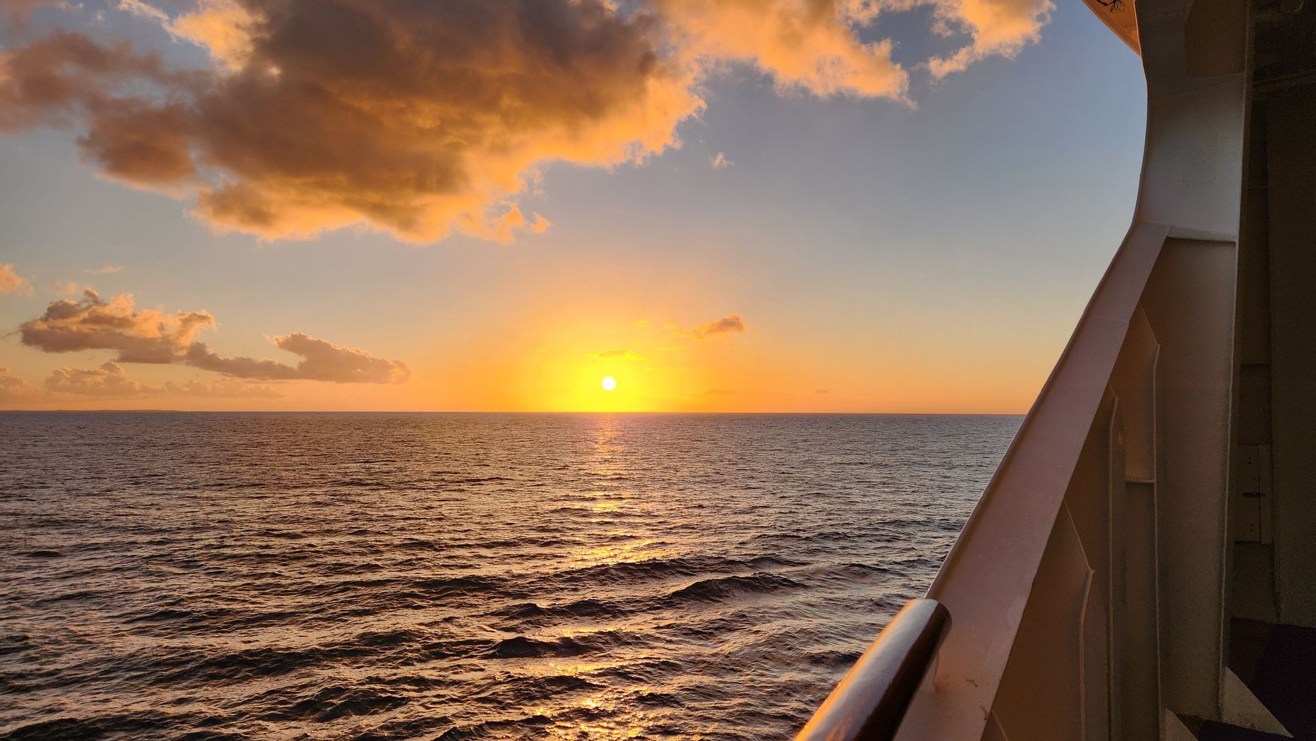 Life preserver ring, white with red stripes, hangs on a metal railing against a clear blue sky.