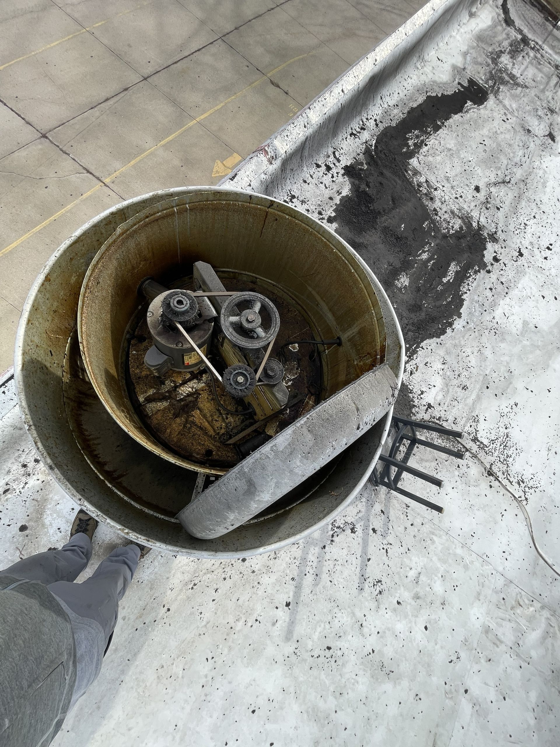 Overhead view of a cylindrical industrial fan unit on a roof, covered in black debris and an impeller blade.