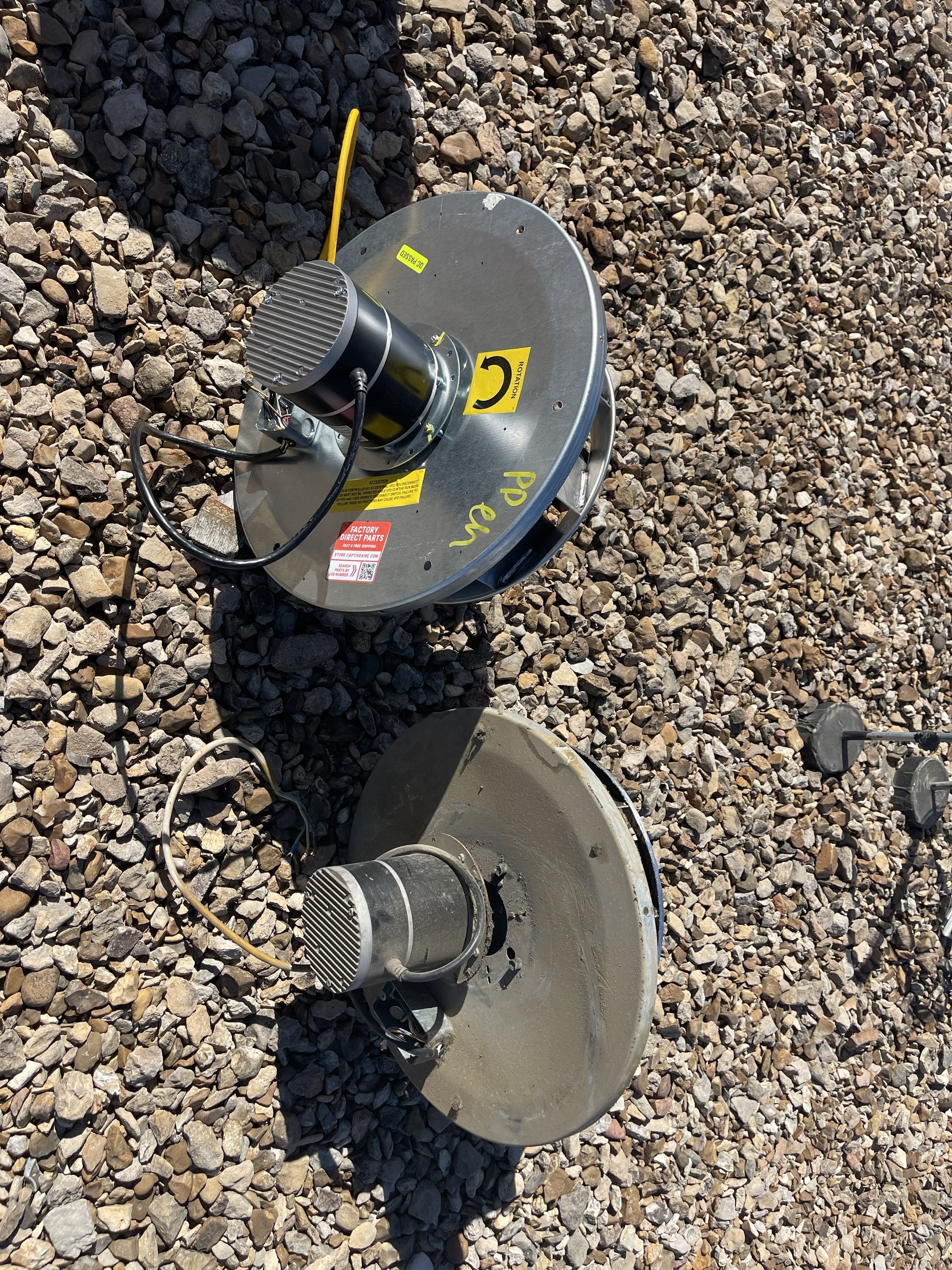 Two circular metallic objects with wire connections and mesh tops, on gravel.