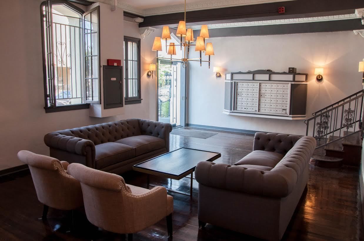 Lobby with tufted sofas, armchairs, and a coffee table, under a chandelier, with a staircase.