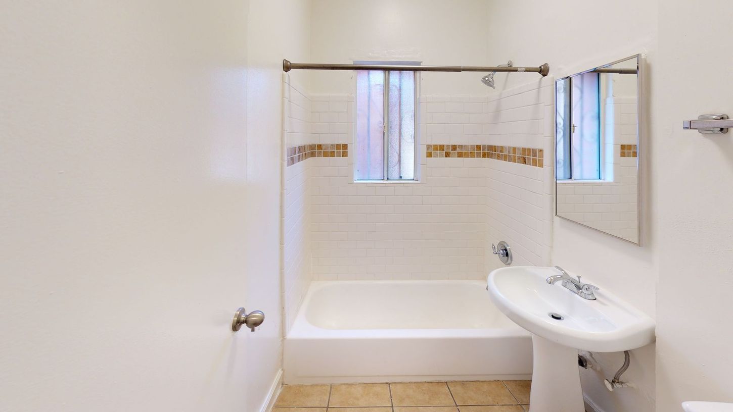 Bathroom with white tub, sink, and walls, small window with brown tile accents.