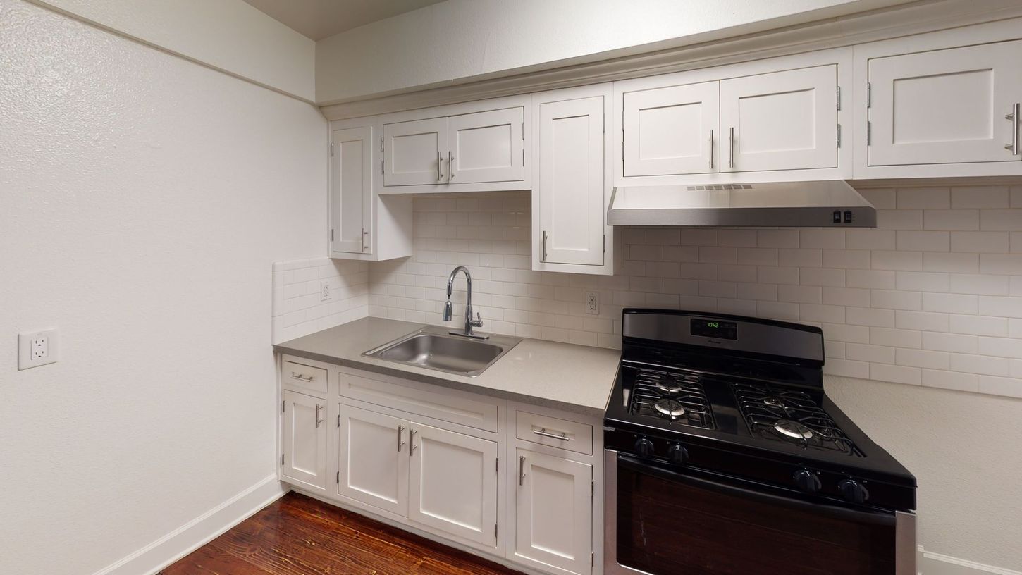 Small kitchen with white cabinets, silver sink, and black stove.