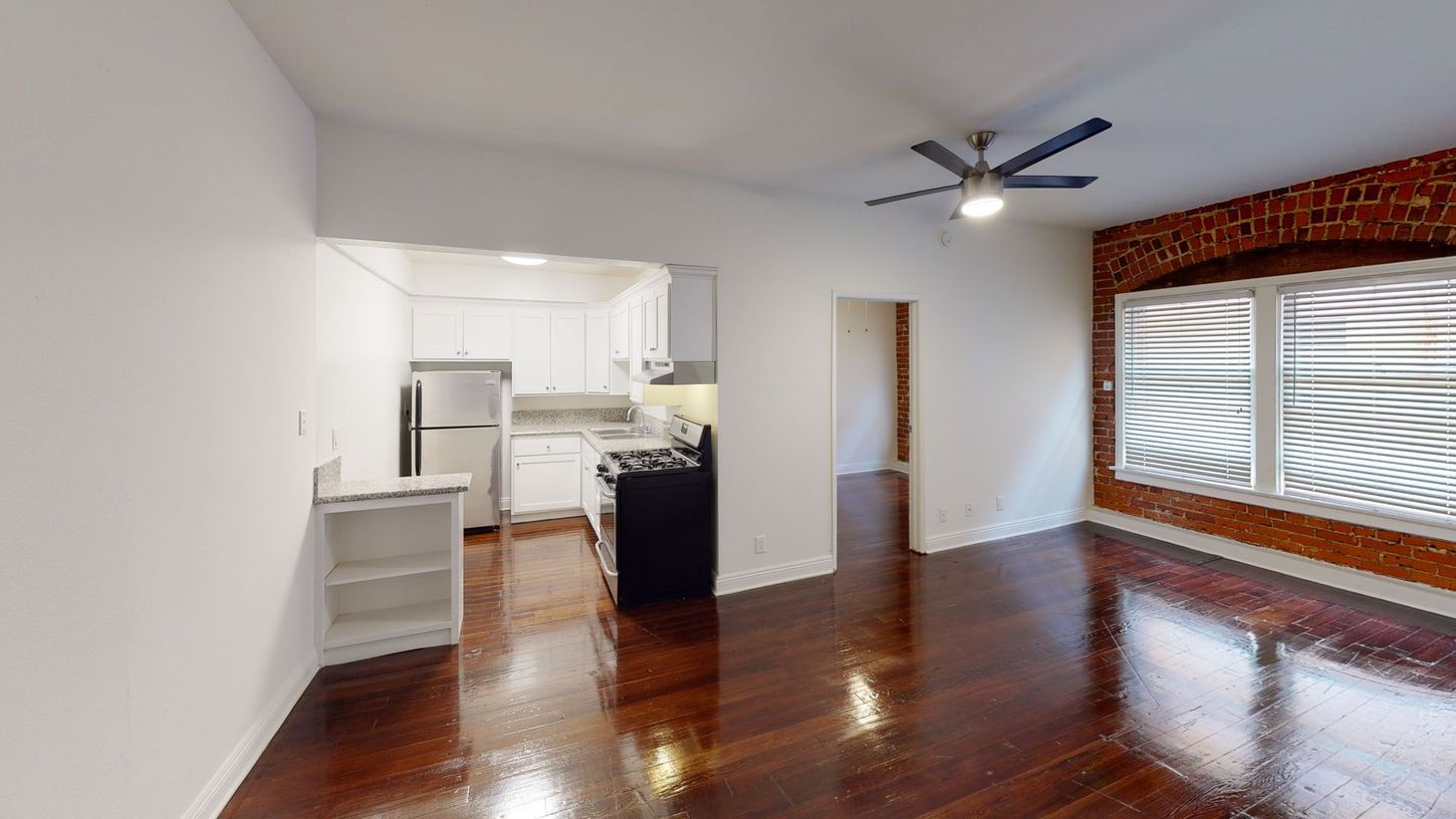 Interior apartment with exposed brick wall, dark wood floors, and kitchen visible.