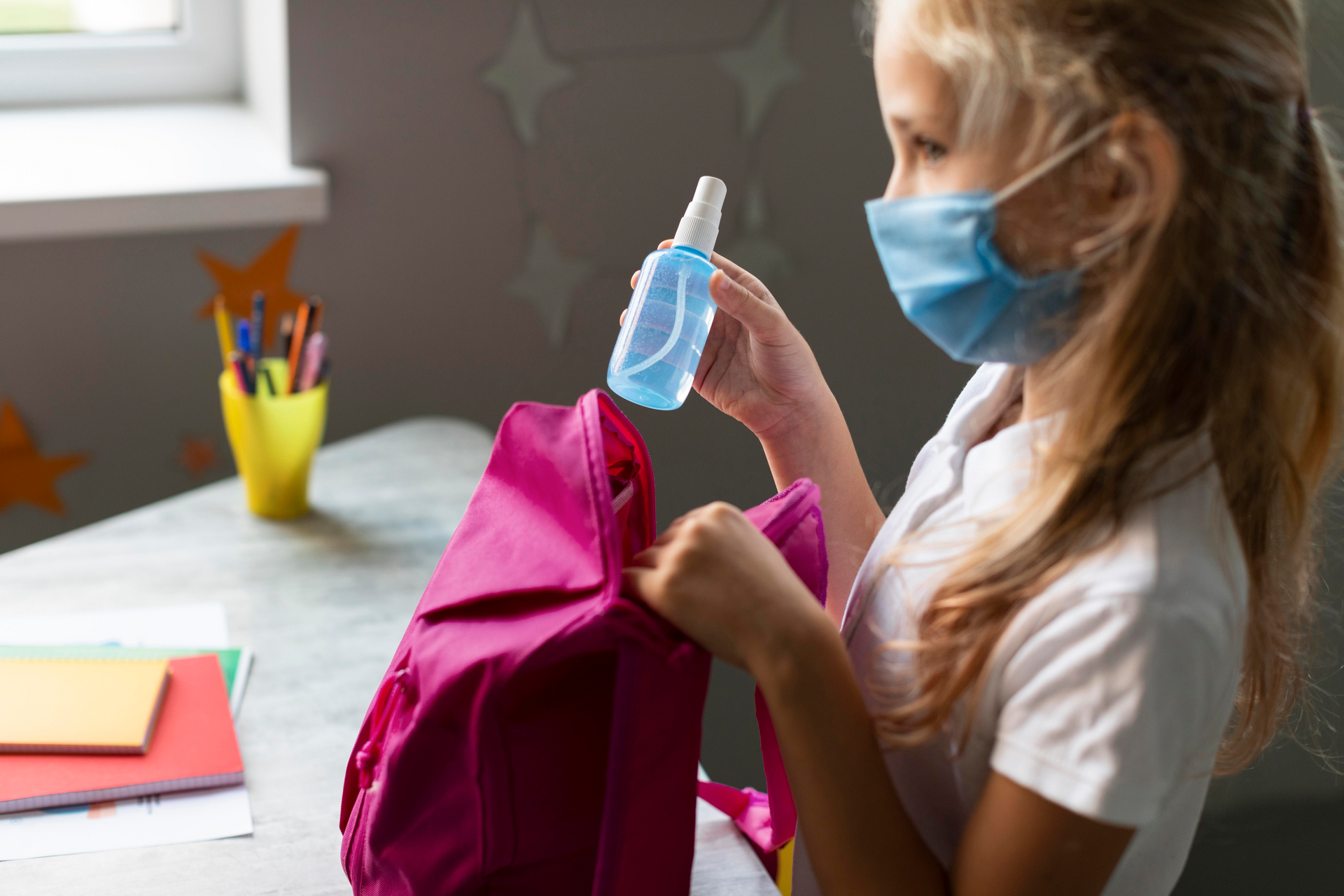 A child wearing a face mask and putting hand sanitizer on her bag