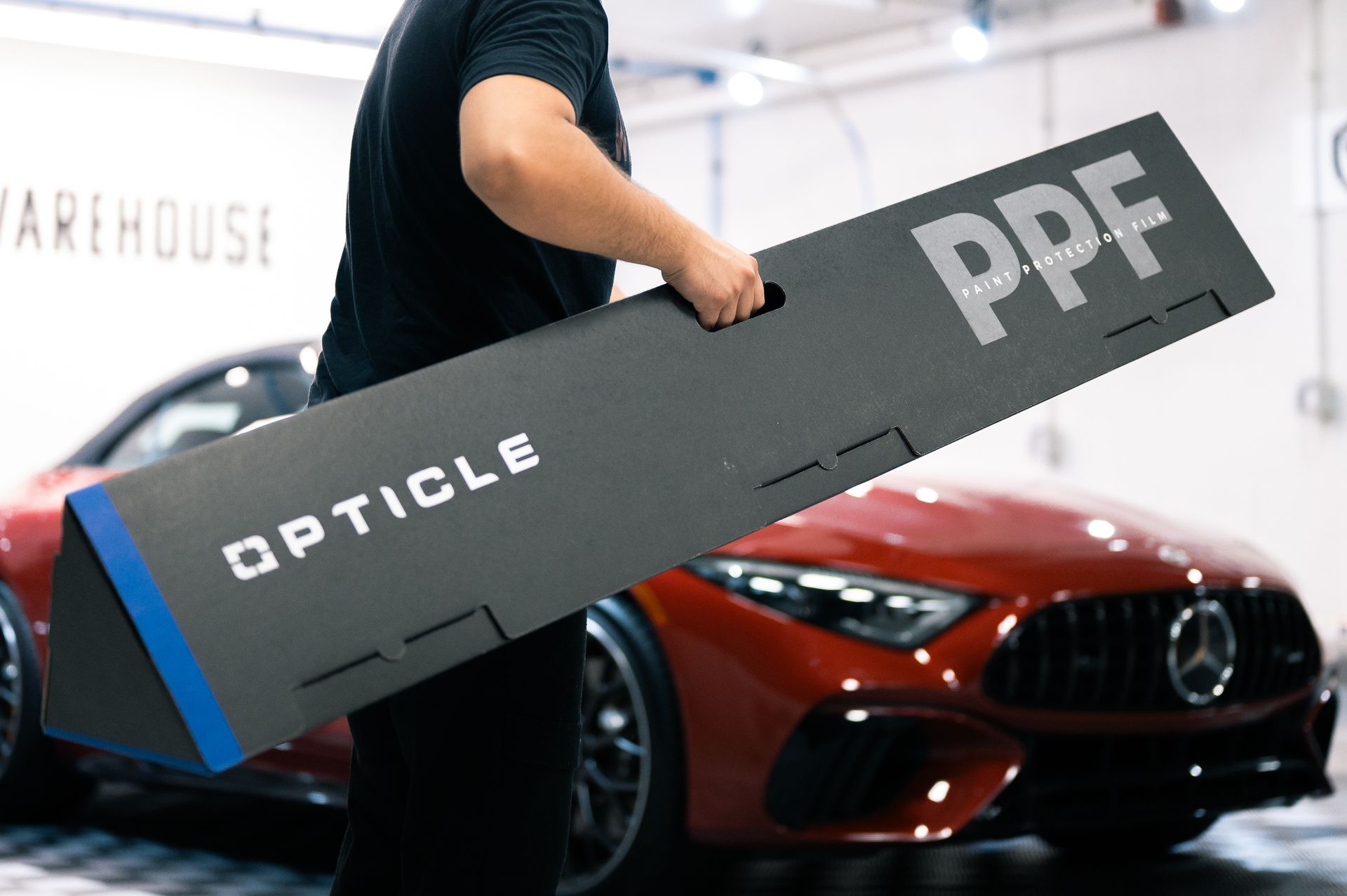 A man is holding a large piece of cardboard in front of a red car.