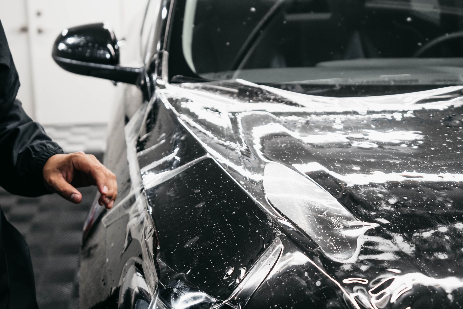 A person is applying a protective film to a black car.