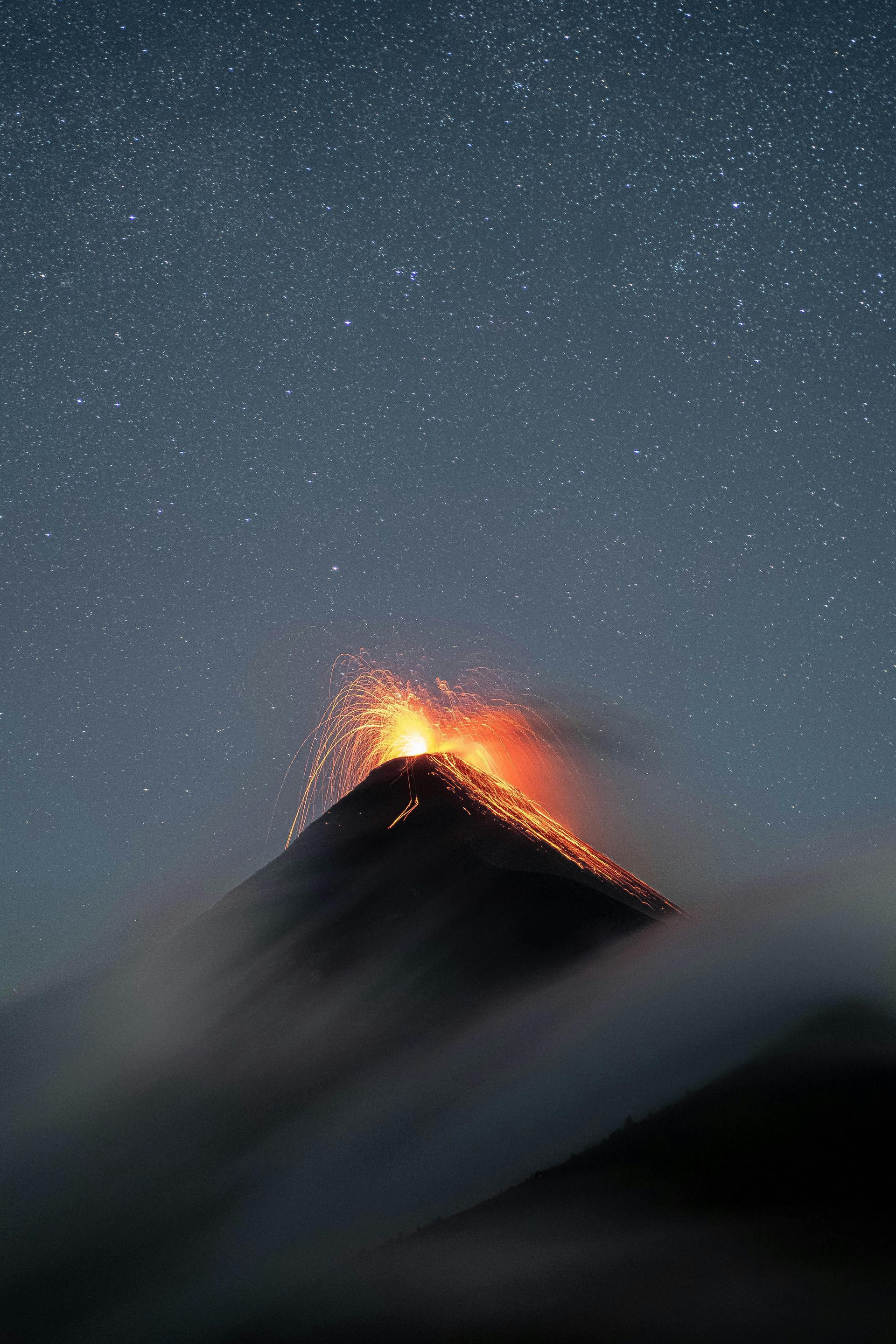 Volcano erupting at night, spewing lava and smoke, with a starry sky.