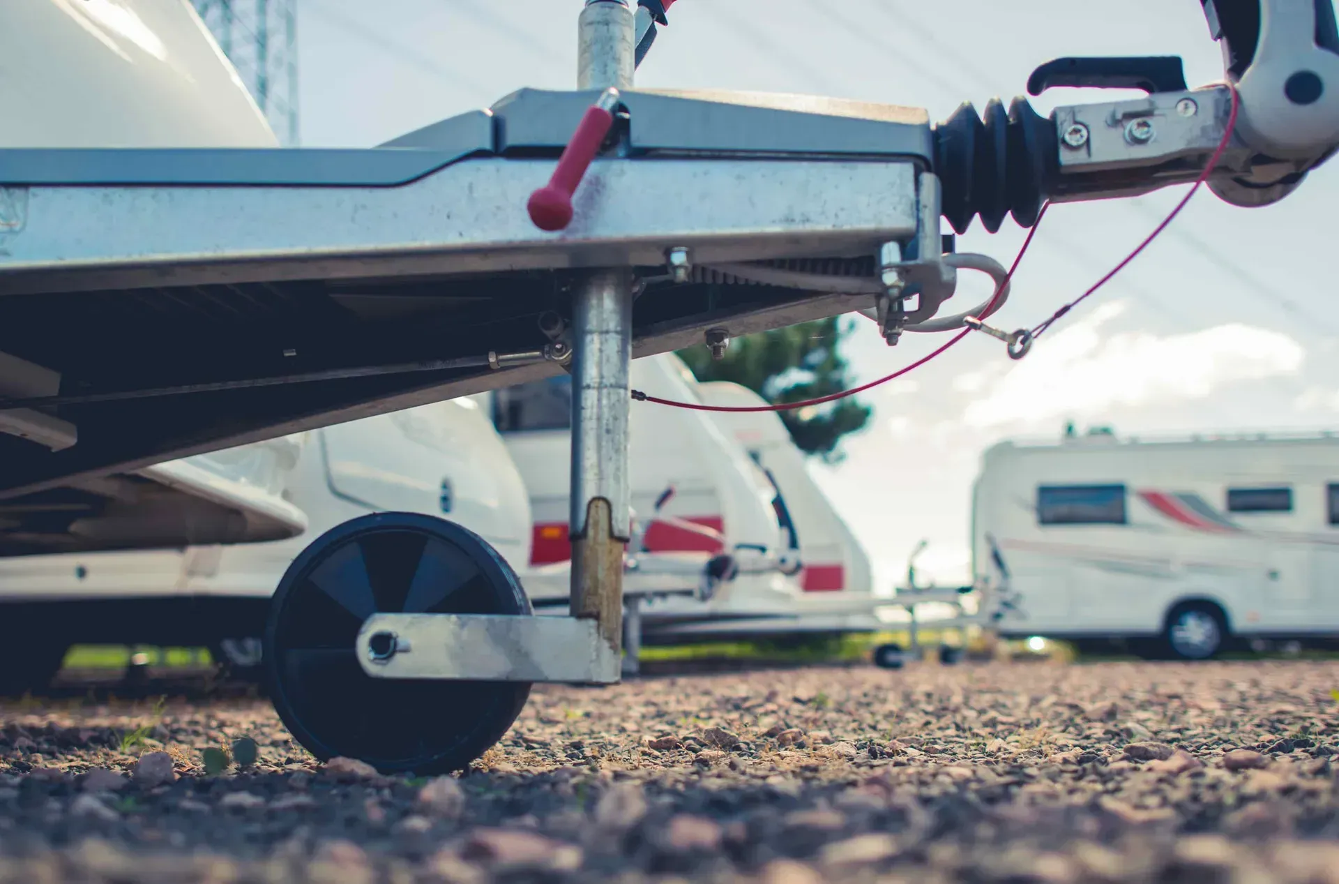 A trailer is parked in a gravel lot next to a row of camper vans.