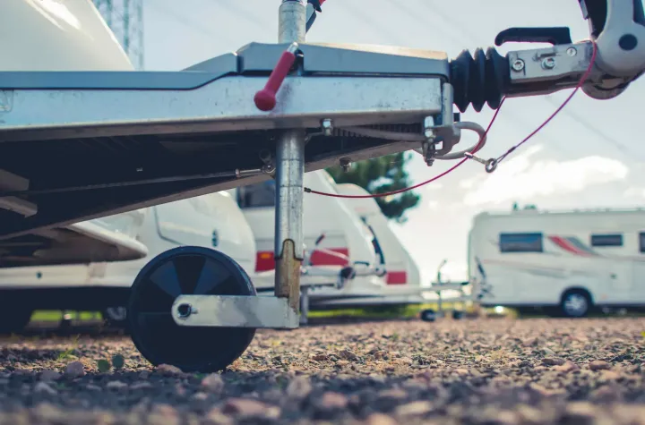 A trailer is parked in a gravel lot next to a row of camper vans.
