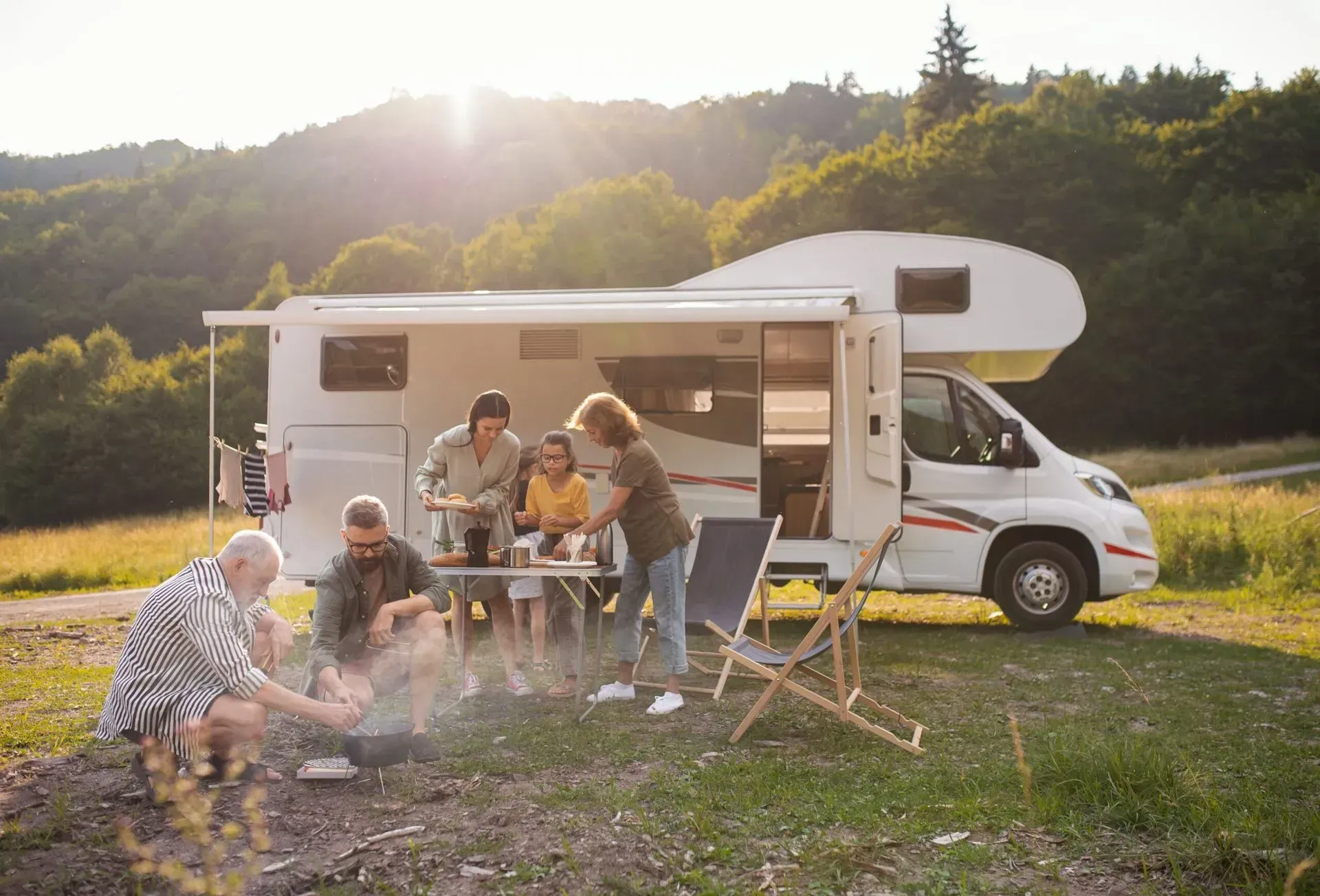 A group of people are sitting around a campfire in front of a rv.
