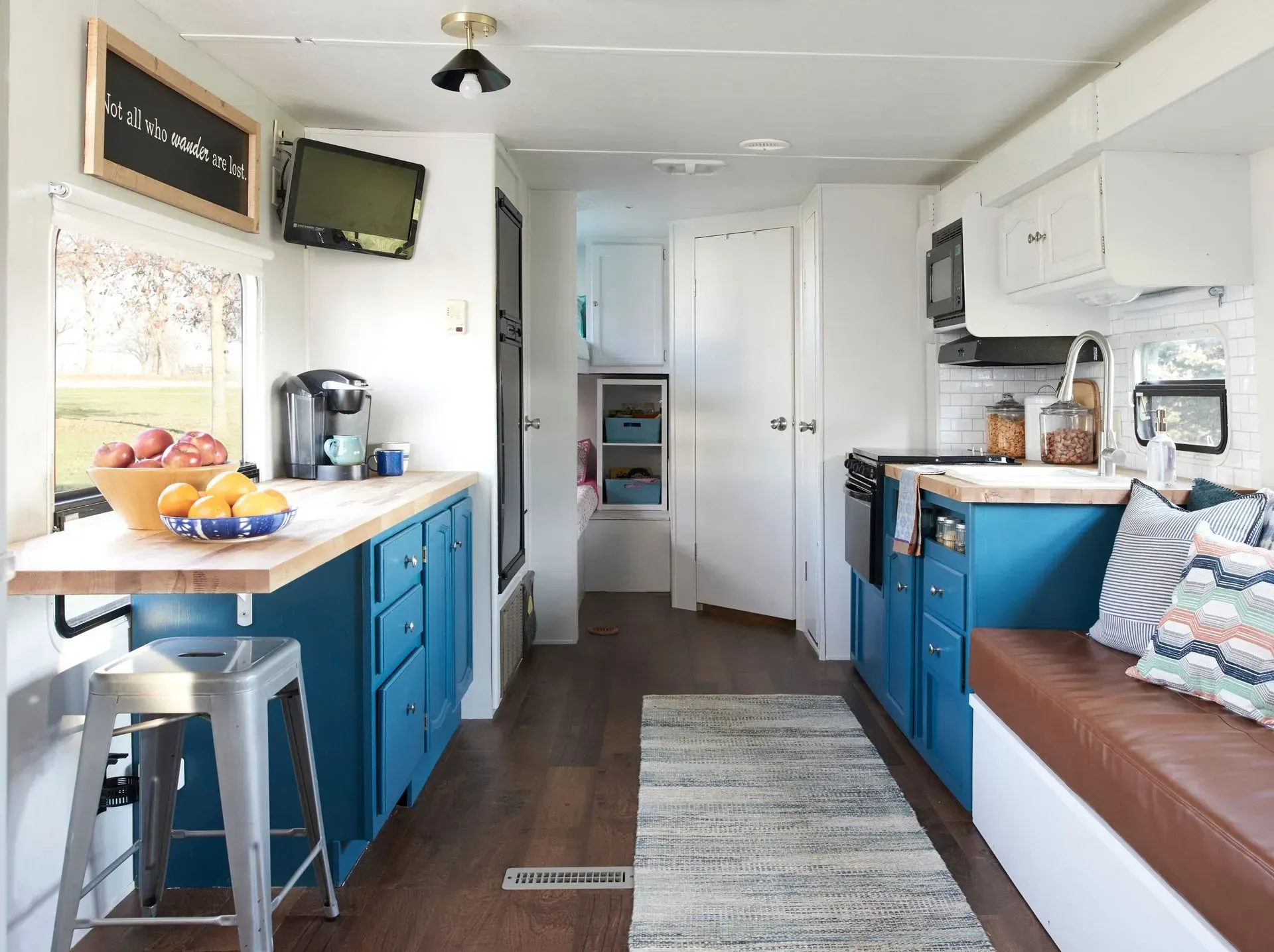 A kitchen in a trailer with blue cabinets and a couch.