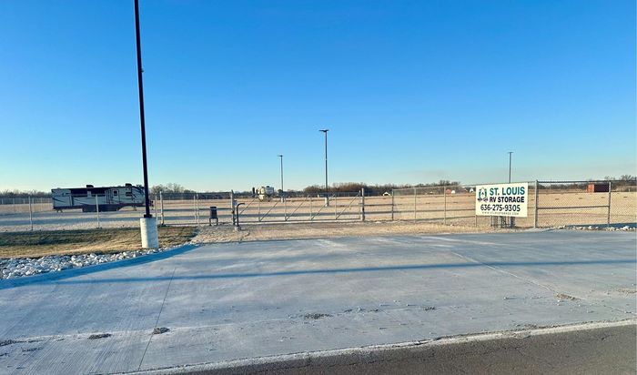 A snow-covered parking lot on a clear, blue-sky day with a few light poles and a sign.