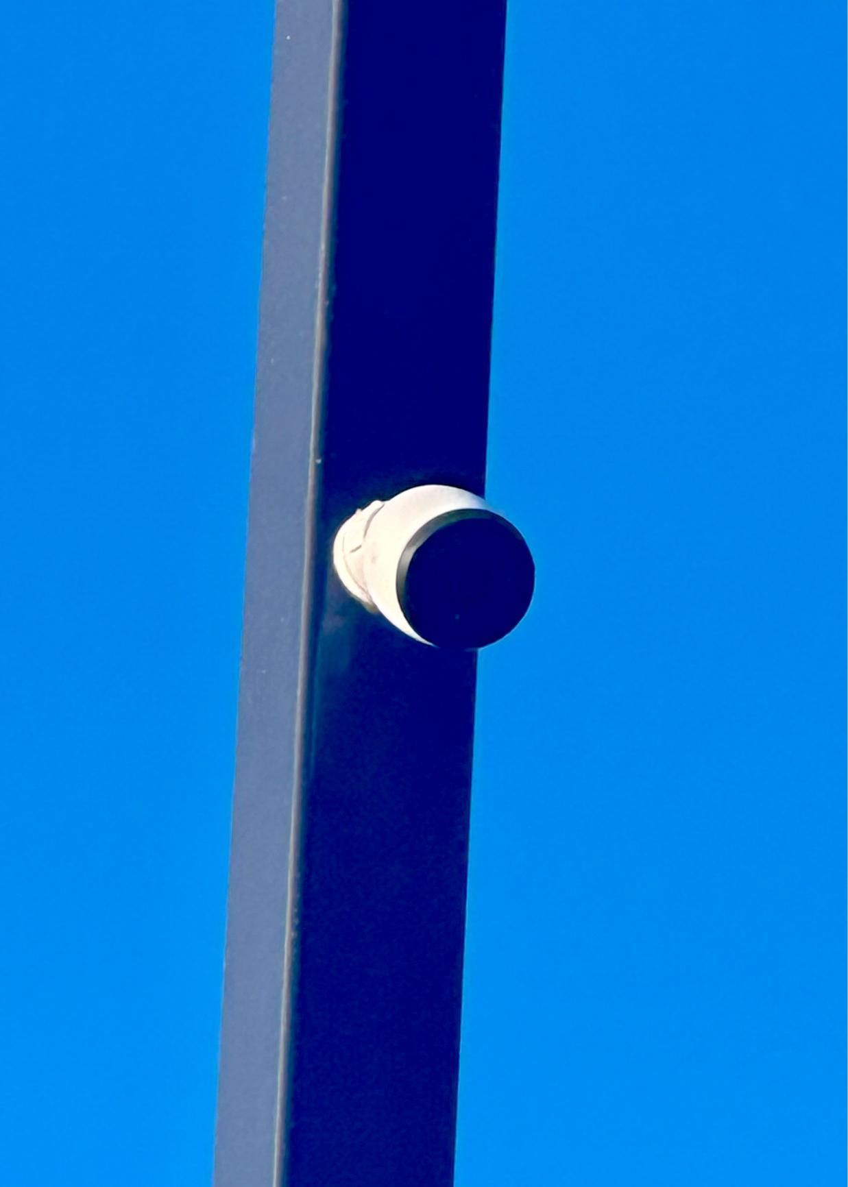 Dark blue metal pole with a white and black cylindrical component against a blue sky.