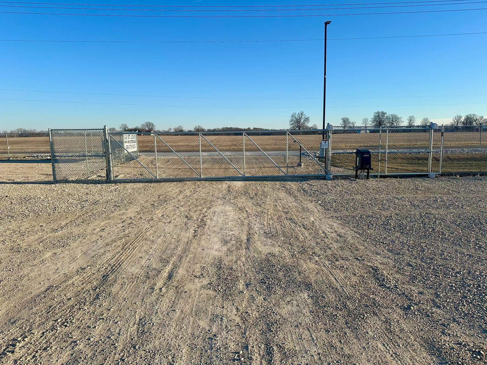 Gravel driveway leading to a gated field under a clear blue sky.