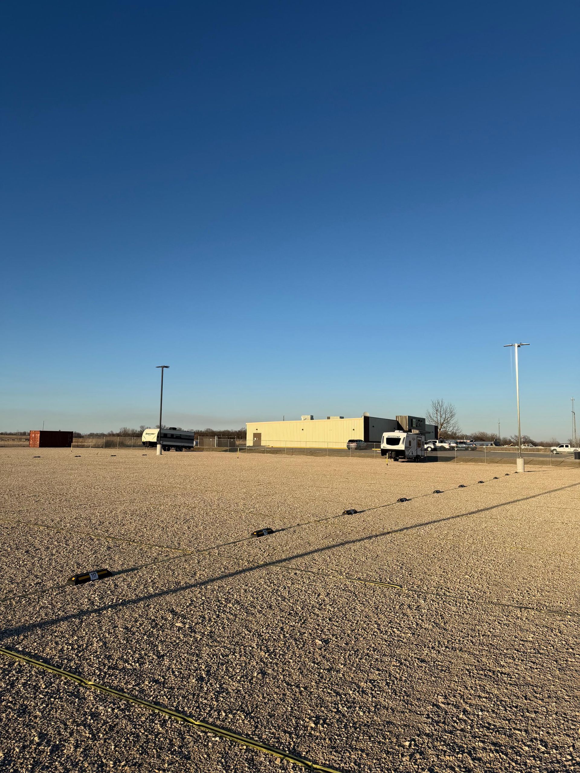 Gravel lot with RVs and a building under a clear blue sky.