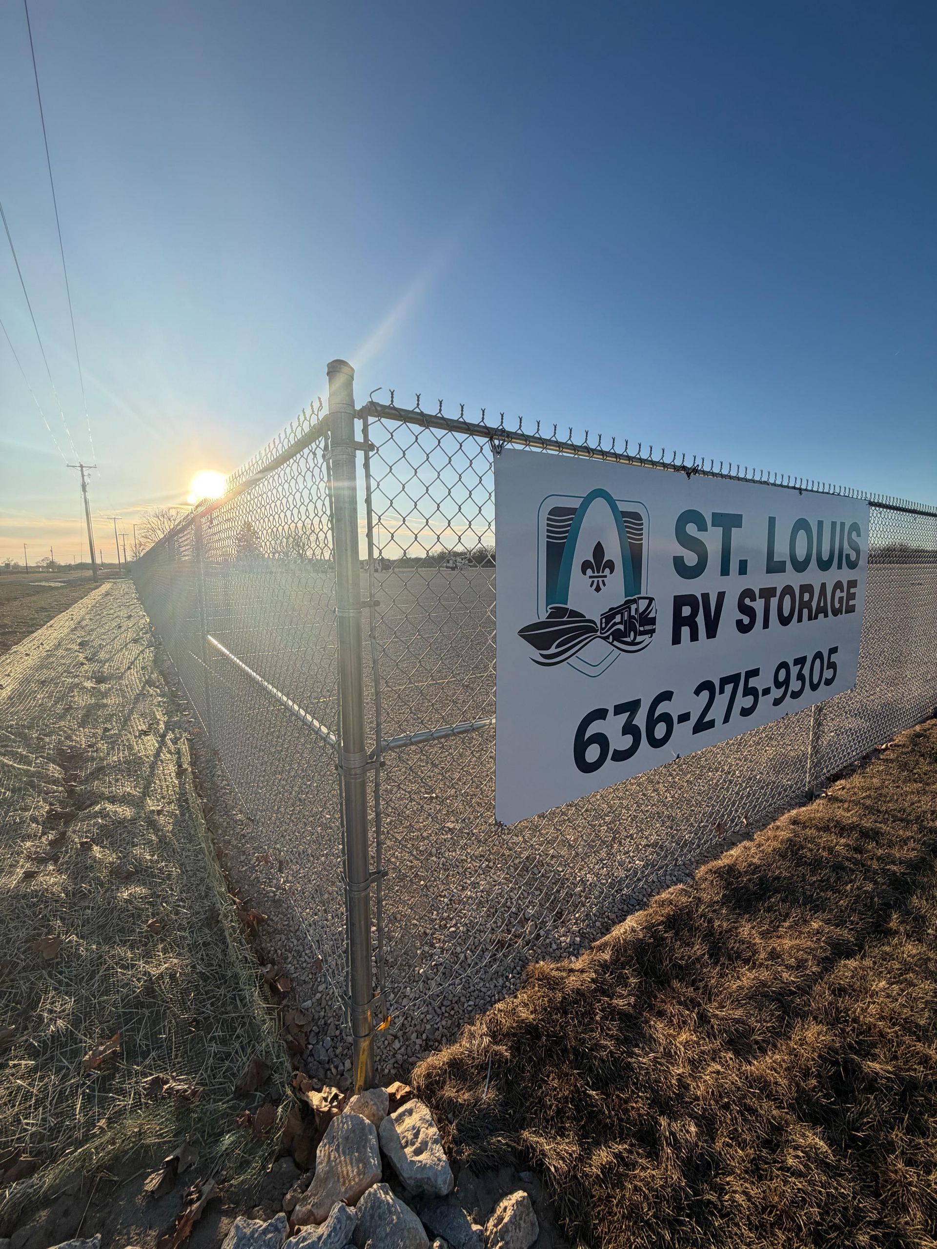 Sign for St. Louis RV Storage on a chain-link fence, with a bright sun in the background.