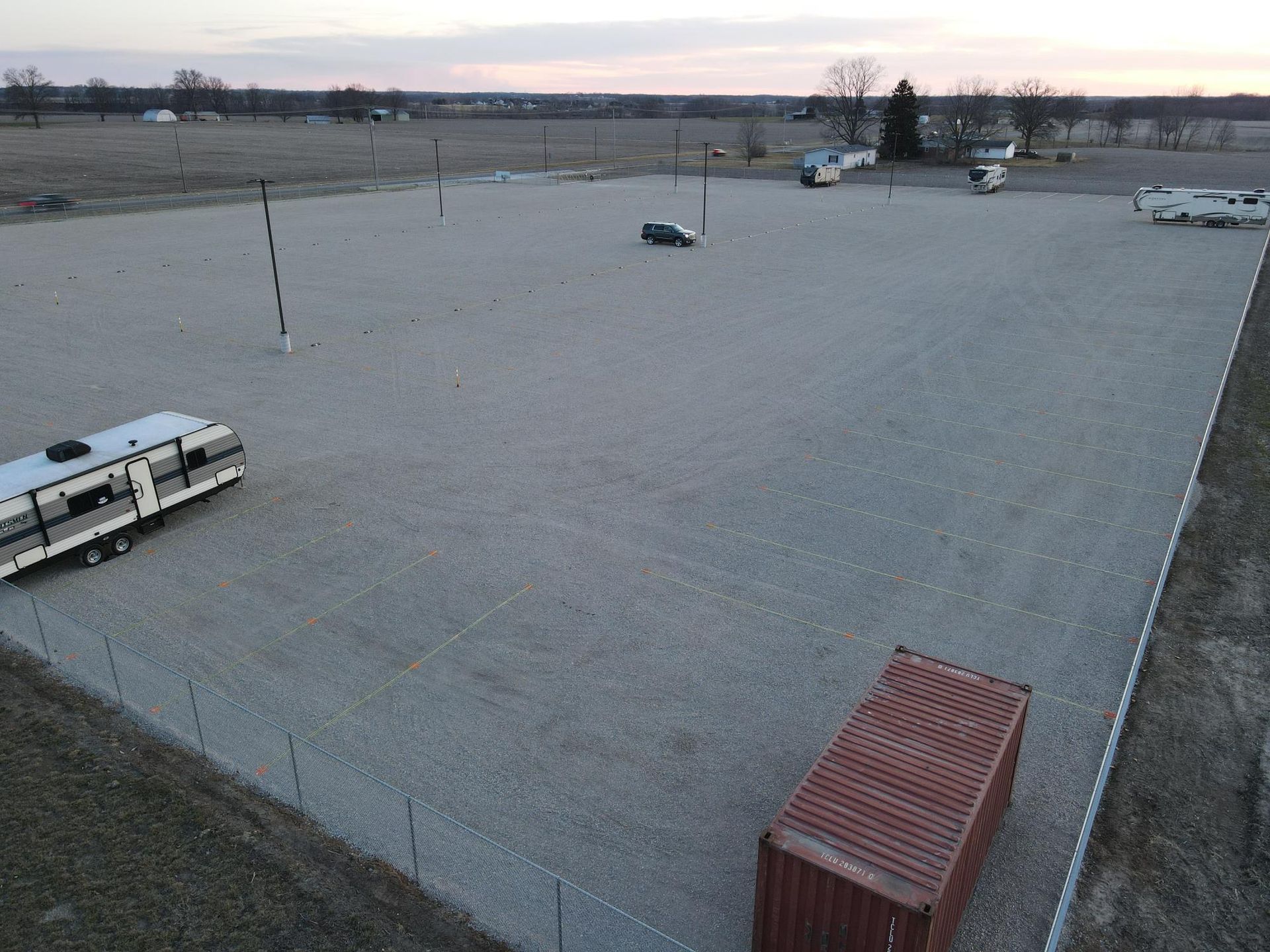 Aerial view of a gravel storage lot with a camper, a shipping container, and a few parked vehicles.