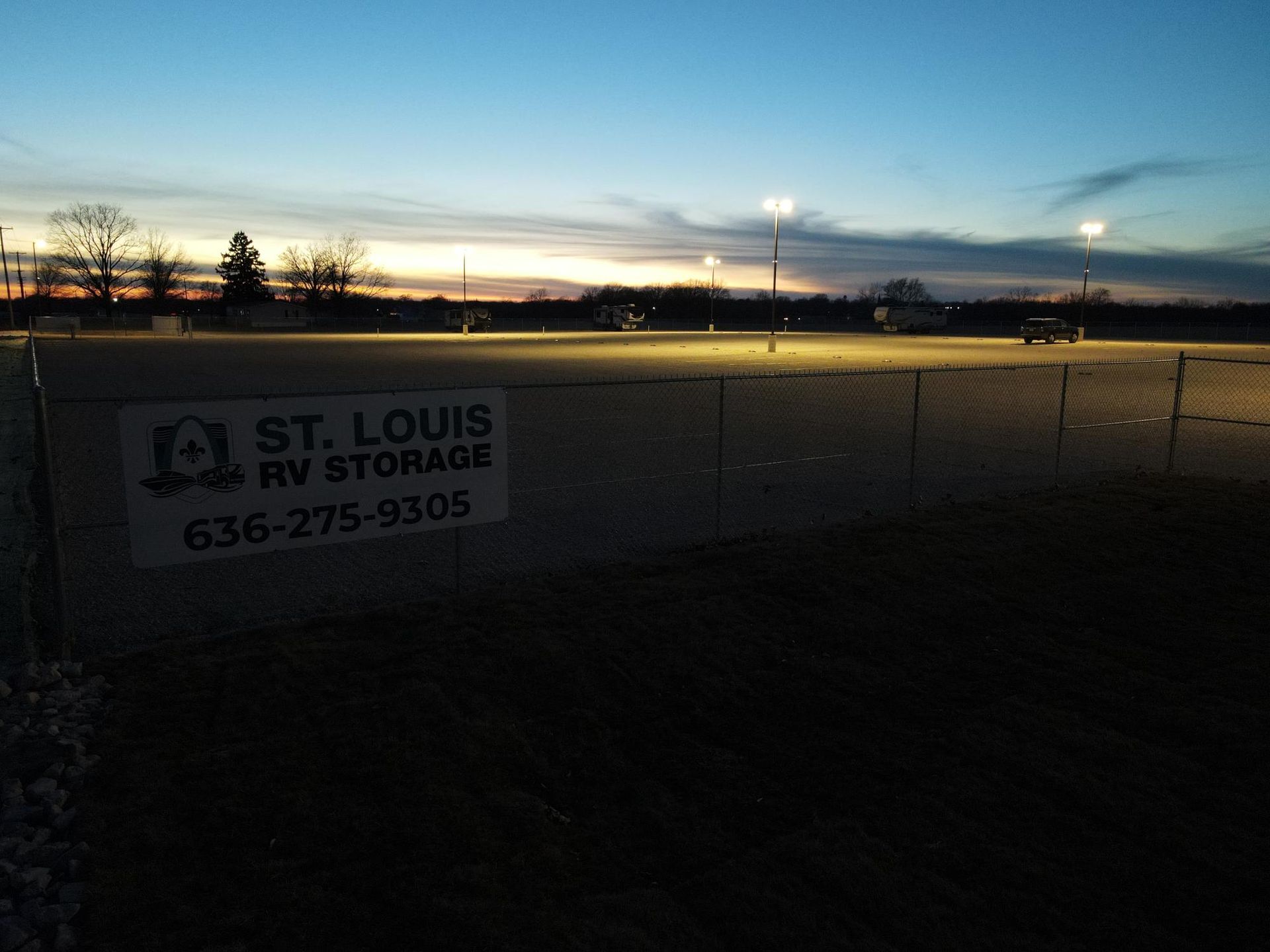 St. Louis RV Storage sign on a fence at a dusk-lit storage lot with parking lot lights.