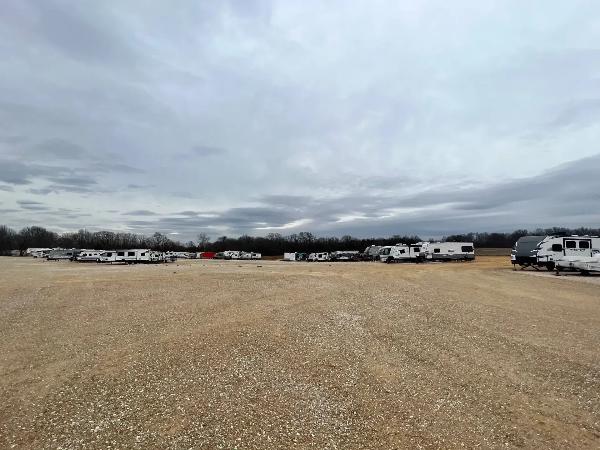 A row of rvs are parked in a gravel lot.